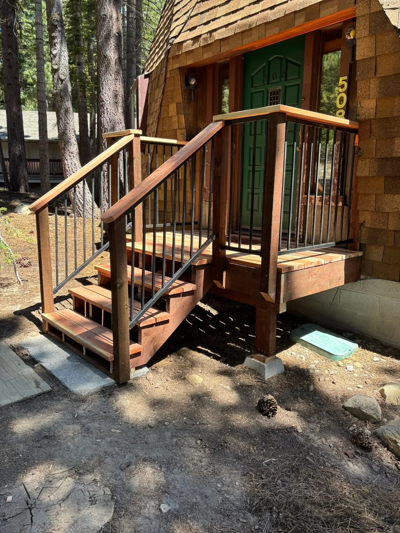 Redwood deck with metal balusters, custom handrails, and brick steps leading to home entrance