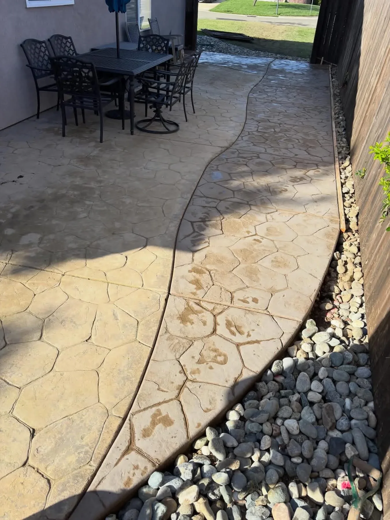 Stamped hexagonal concrete patio with tan and gray tones, river rock border edging