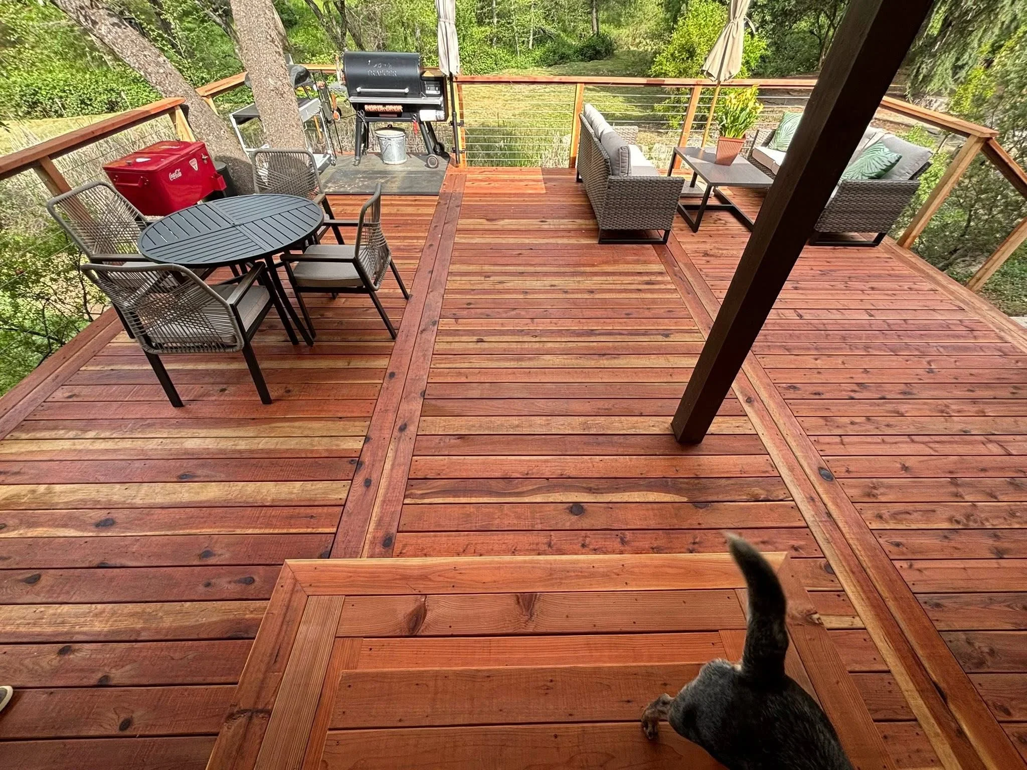 Wooden deck with cable railing, multiple levels, and covered patio area surrounded by trees