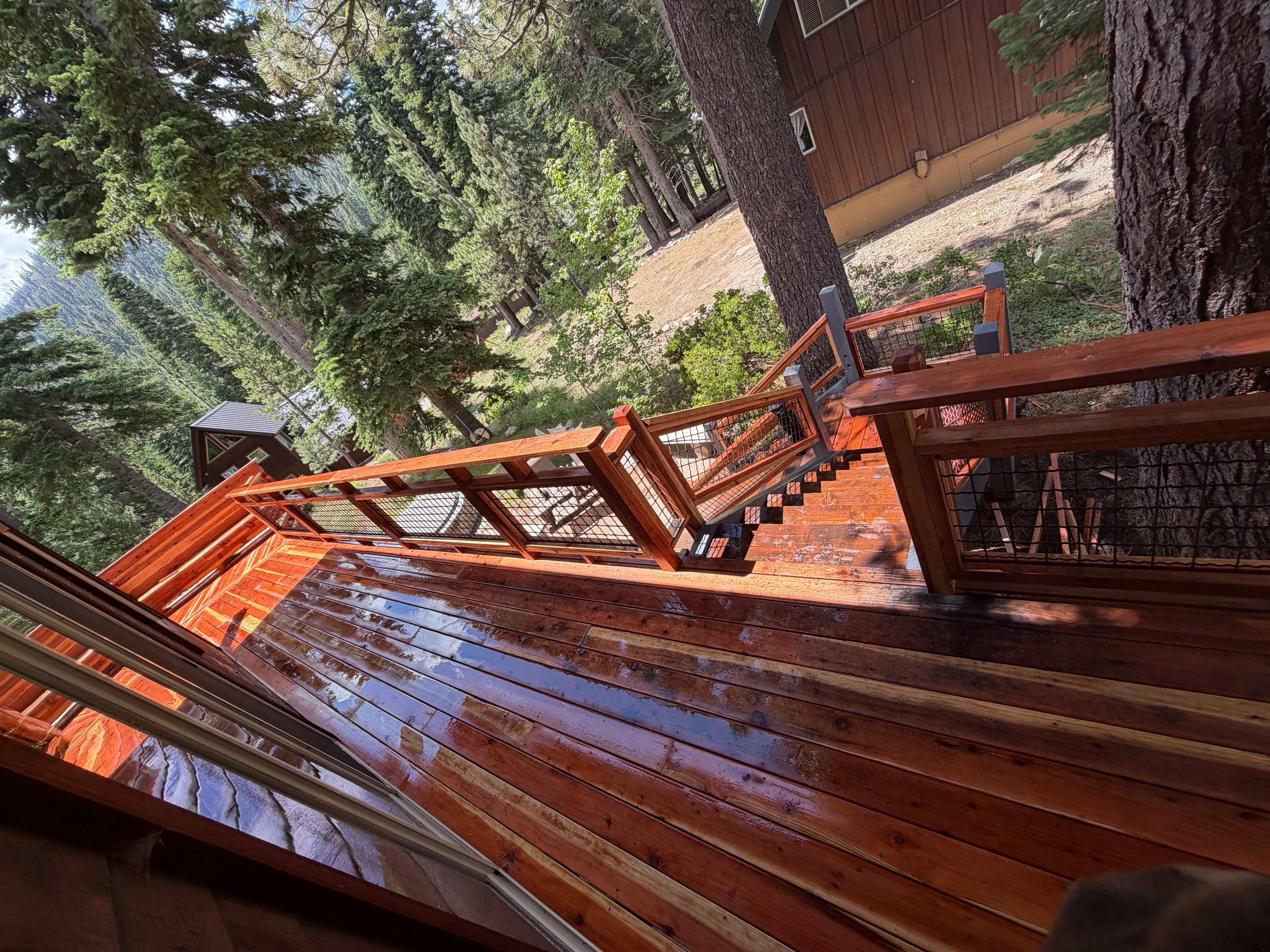 Multi-level redwood deck with metal railings and pergola, angled construction on slope