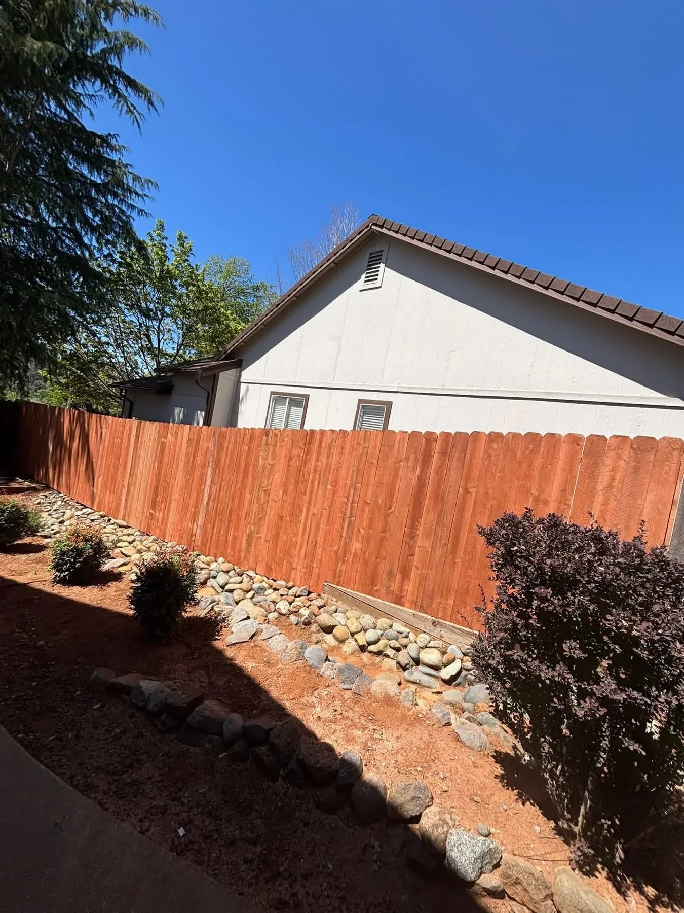 Redwood privacy fence with vertical boards and rock drainage base along residential property