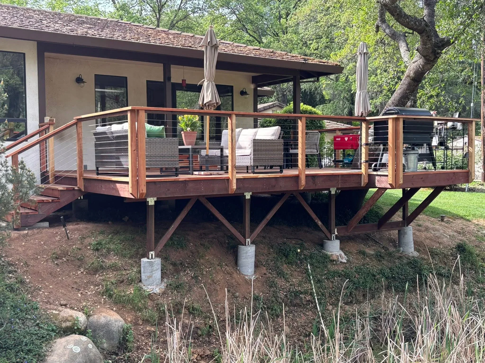 Elevated composite deck with cable railing, wood posts, concrete footings, and integrated stairs