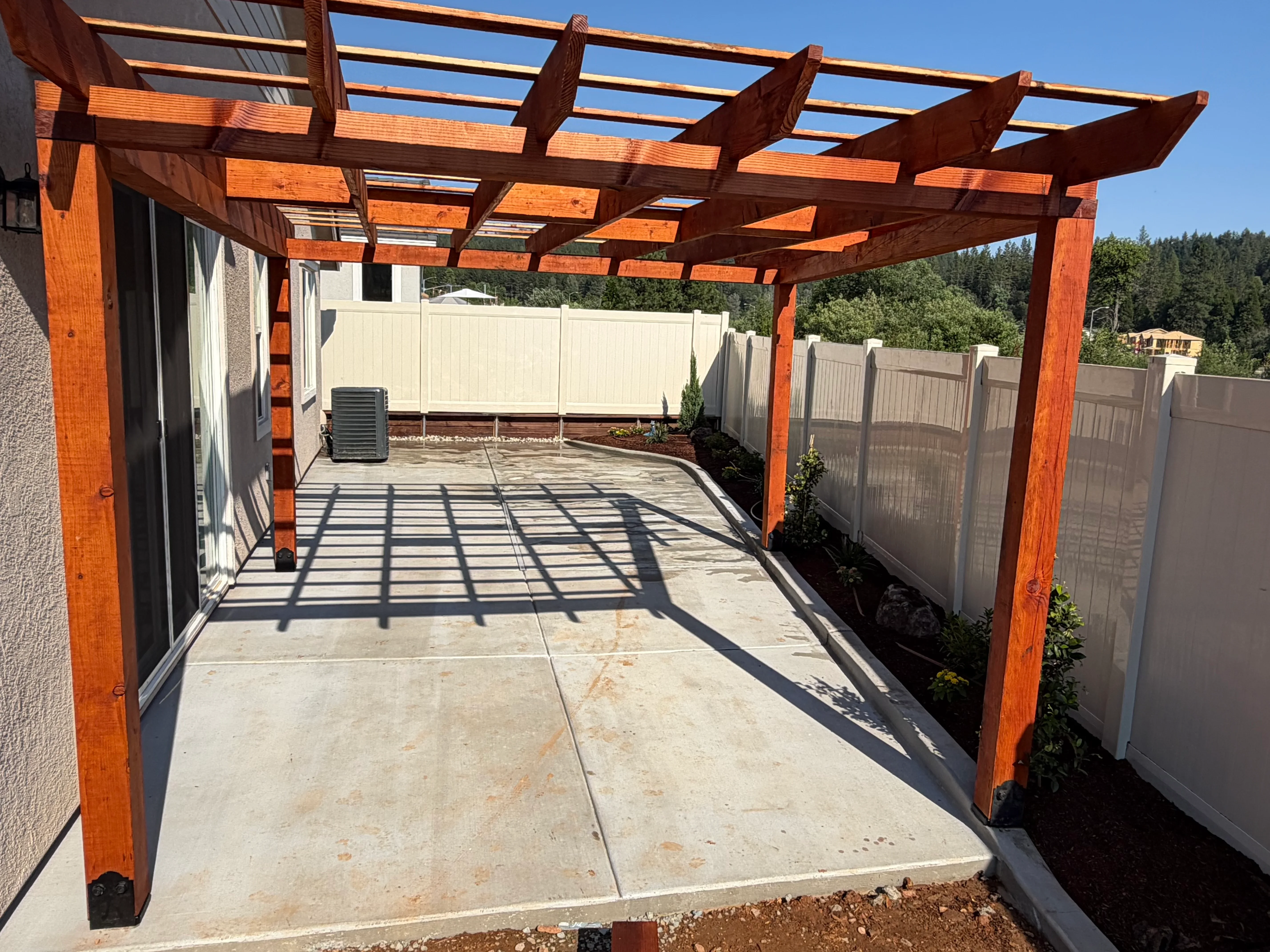 Cedar pergola with lattice roof over concrete patio with vinyl fence enclosure