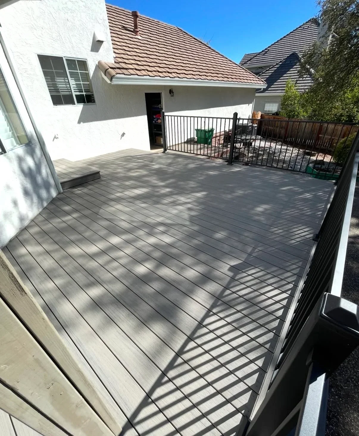 Gray composite deck with black metal railing attached to white house with clay tile roof