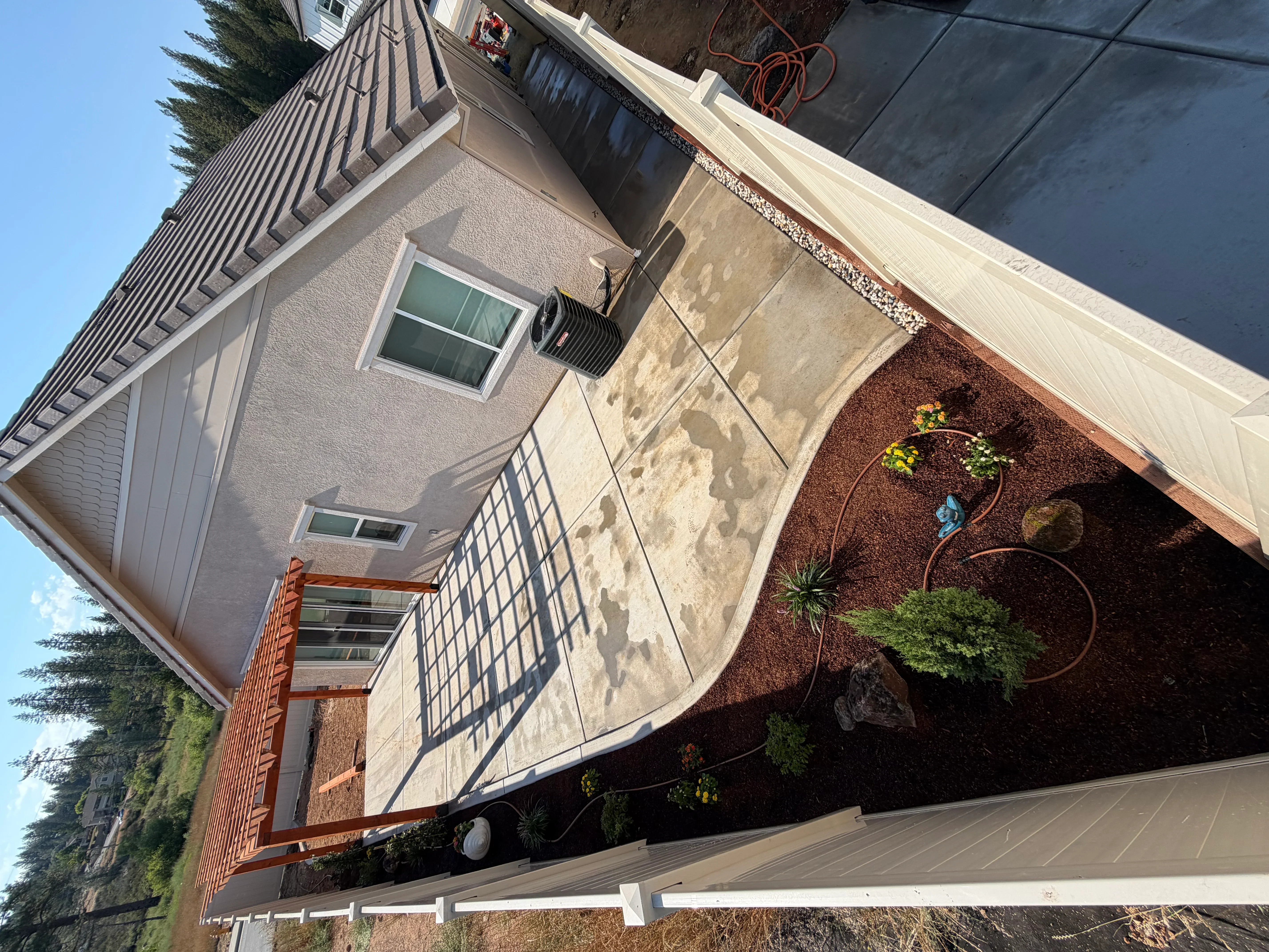 Concrete patio with mulch landscaping beds and metal garden features adjacent to brick home