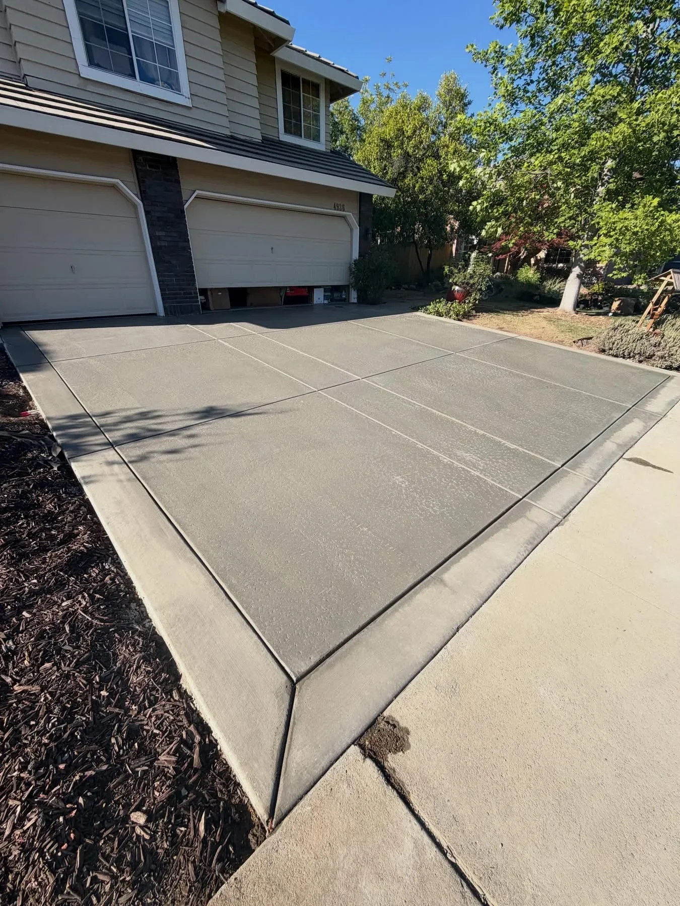 Newly poured concrete driveway with control joints and finished edges adjacent to two-car garage