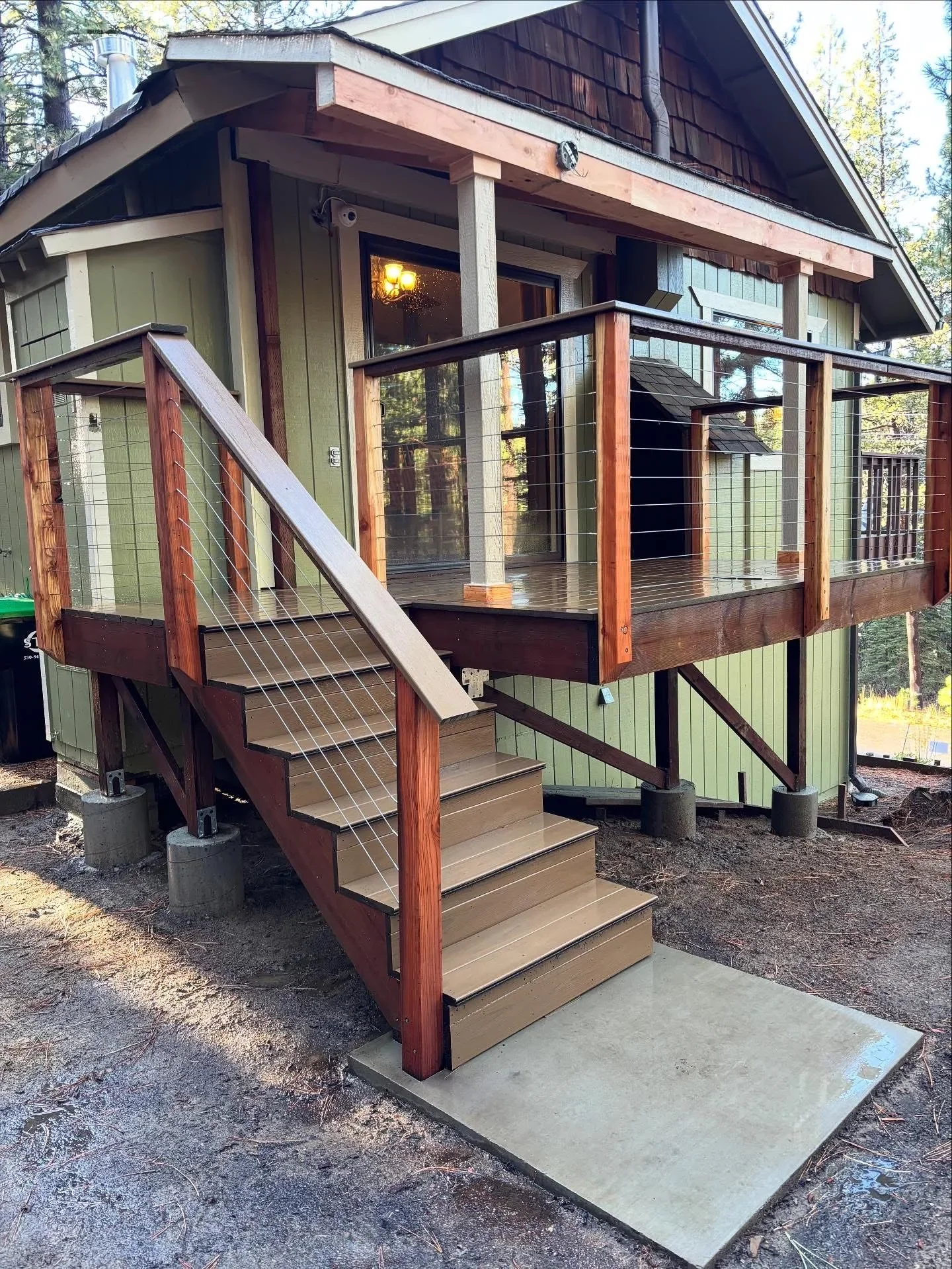 Elevated composite deck with cable railing, wooden stairs, and covered porch with glass panels