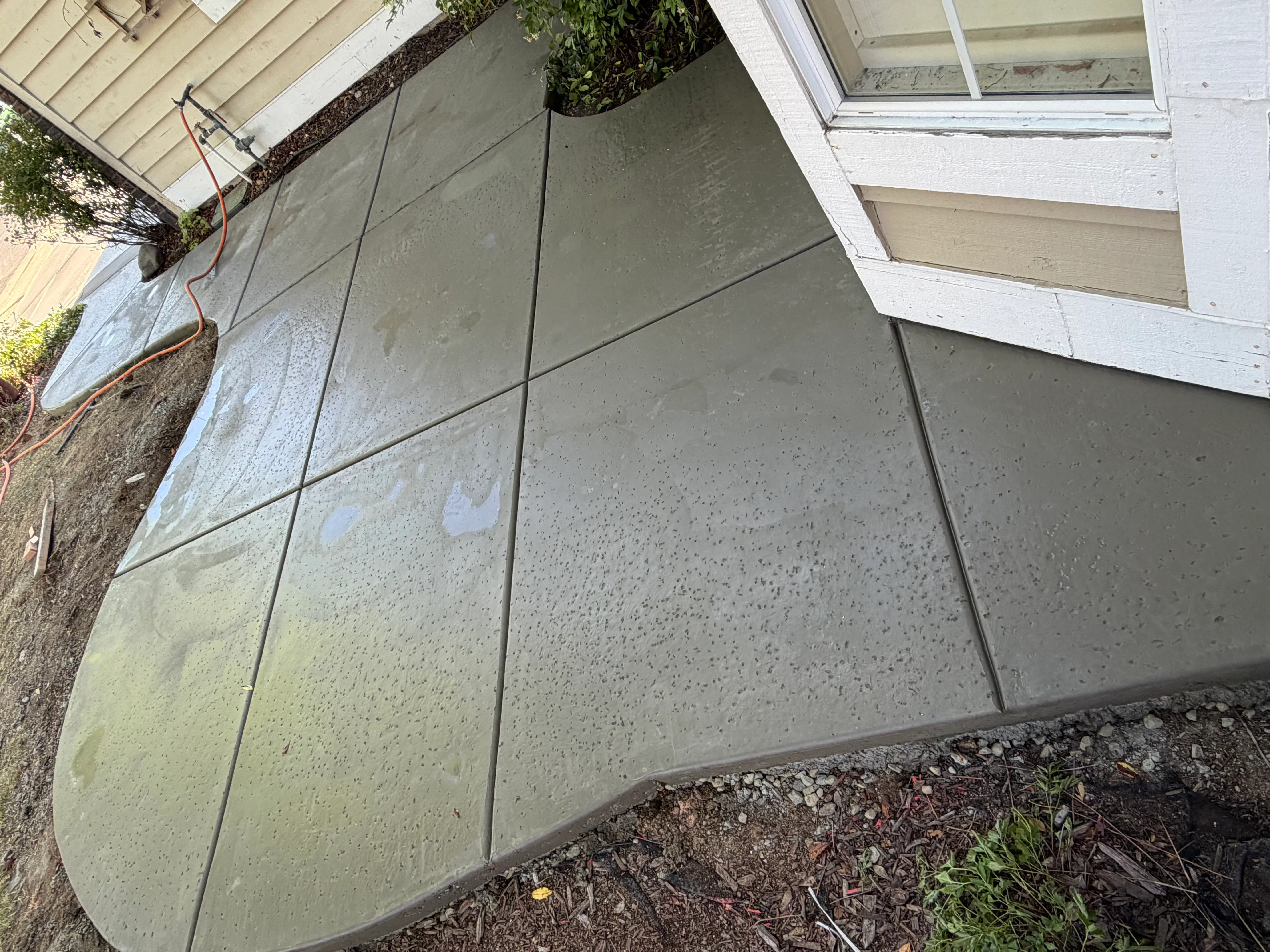 Finished concrete patio with control joints and aggregate surface near home foundation