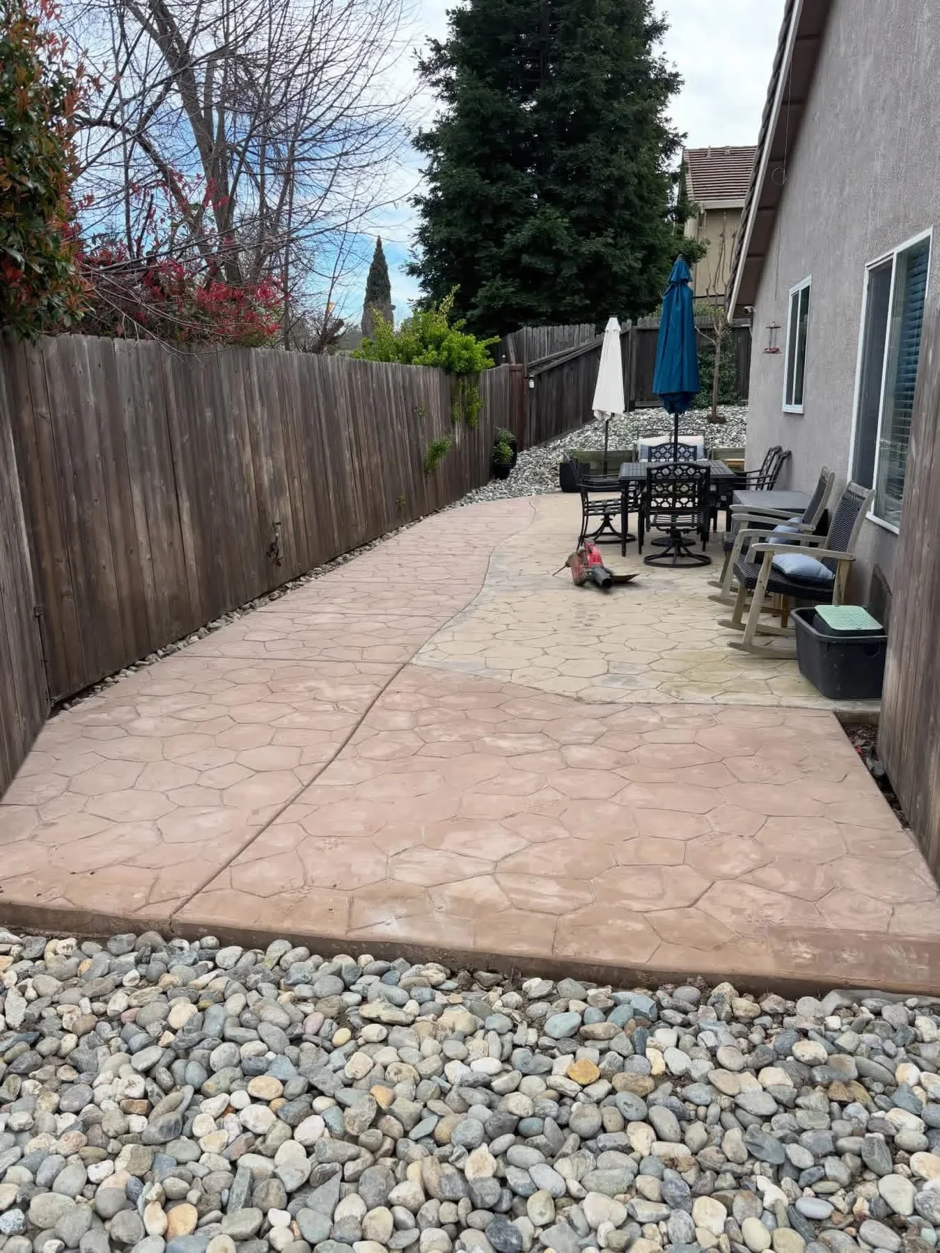 Stamped concrete patio with stone pattern, river rock border, wooden fence, and outdoor furniture